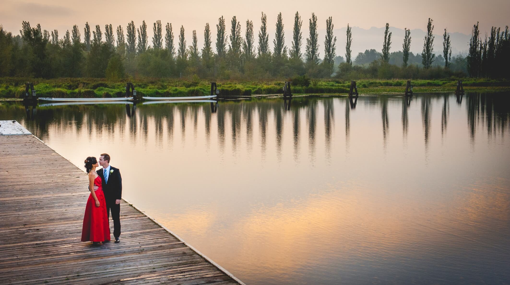 Couple standing on the dock by a lake at dusk.