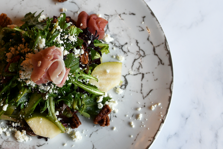 A picture of a plate of salad with prosciutto and pear
