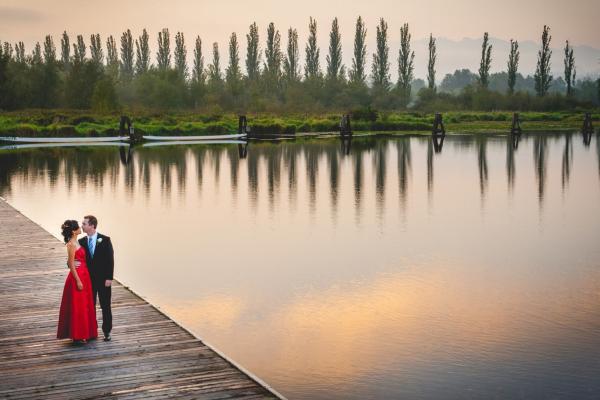 Couple standing on the dock by a lake at dusk.